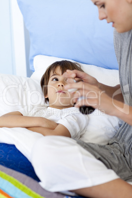 Mother giving her son lying in bed syrup