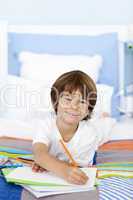 Smiling little boy drawing in bed