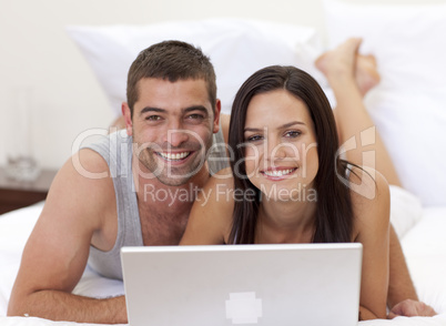 Smiling couple in bed using a laptop
