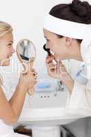 Daughter holding a mirror and mother putting makeup