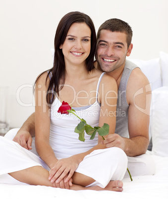 Couple sitting on bed with a rose