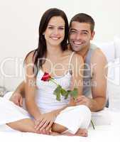 Couple sitting on bed with a rose