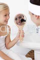 Smiling daughter holding a mirror and mother putting makeup