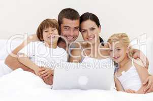 Portrait of family using a laptop in bed