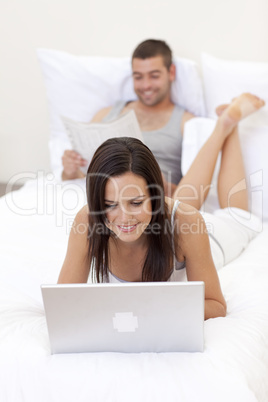 Couple in bed with a laptop and reading a newspaper