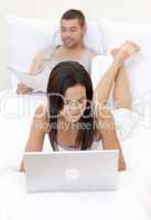 Wife using a laptop and husband reading a newspaper