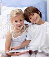 Happy brother and sister reading a book in bedroom