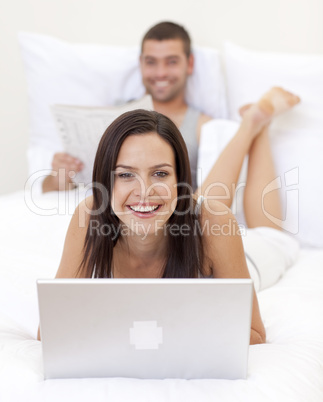 Smiling woman using a laptop and man reading a newspaper