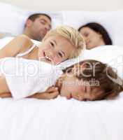 Little girl smiling on bed wile her family sleep