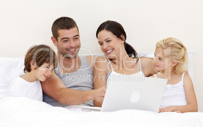 Parents and children using a laptop in bed