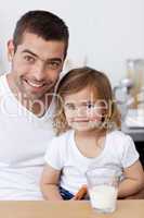 Smiling dad and little girl eating biscuits with milk
