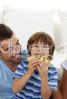 Boy eating pizza in living-room with his father