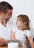 Father reading a newspaper smiling to his daughter