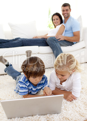 Children using a laptop and couple lying on sofa