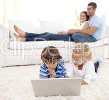 Children using a laptop and parents lying on sofa