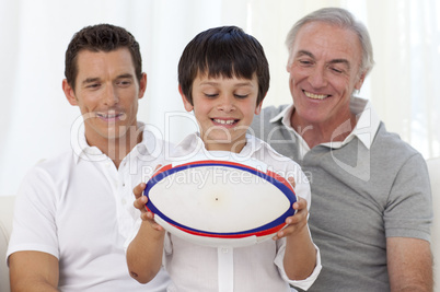 Son holding a rugby ball with his father and grandfather