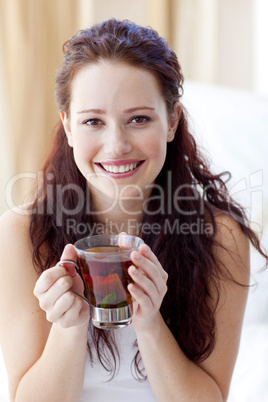 Smiling woman drinking a cup of tea in bedroom