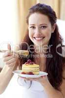 Smiling woman eating pancakes with fruit and honey