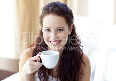 Smiling woman drinking a cup of coffee in bedroom