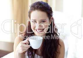 Smiling woman drinking a cup of coffee in bedroom
