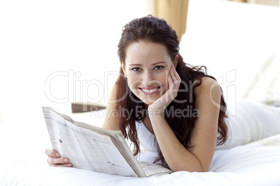 Smiling woman in bed reading a newspaper