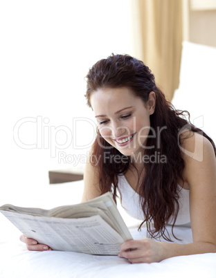 Brunette girl in bed reading a newspaper
