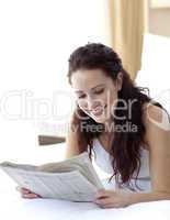 Brunette girl in bed reading a newspaper