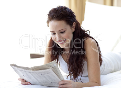 Brunette woman in bed reading a newspaper