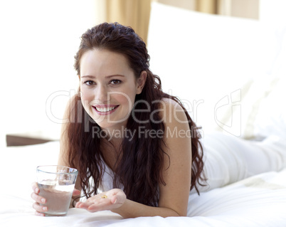 Woman in bed taking pills with water