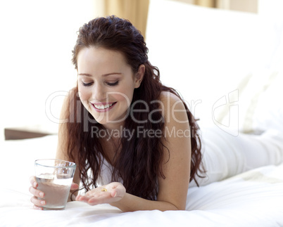 Woman in bed holding a glass of water and pills