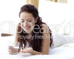 Woman in bed holding a glass of water and pills
