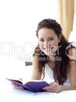 Beautiful woman in bed with a book smiling at the camera