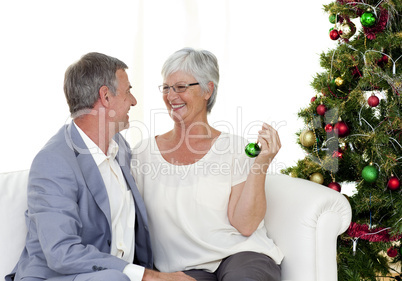 Mature couple sitting on sofa with a Christmas tree