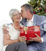 Senior man giving a kiss and a Christmas present to his wife