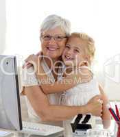 Granddaughter and grandmother hugging and using a computer
