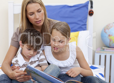 Mother reading a book with her children in bed