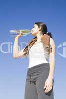 Junge Frau trinkt Wasser nach Sport vorm blauen Himmel