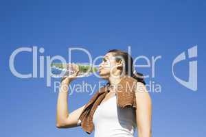 Junge Frau trinkt Wasser nach Sport vorm blauen Himmel