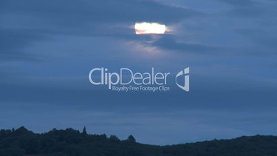 Moon through clouds in blue sky over mountain