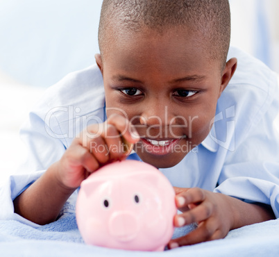 Young Boy on a bed putting money into a piggy bank