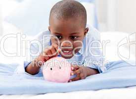 Young Boy on a bed putting money into a piggy bank