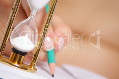 Sand-glass against female hand with pencil