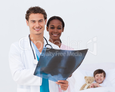 Smiling doctor and nurse examining an x-ray and a kid in bed