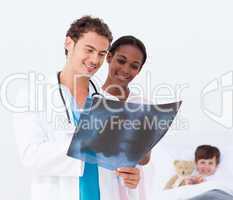 Pediatrician and nurse examining an x-ray and a little patient i
