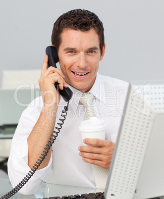 Smiling businessman on phone drinking a coffee in the office