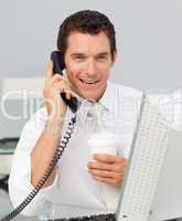 Smiling businessman on phone drinking a coffee in the office