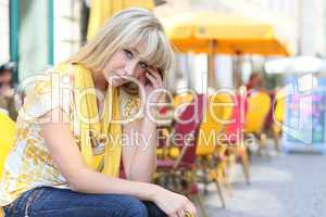 young blond woman is sitting in front of a sidewalk cafe