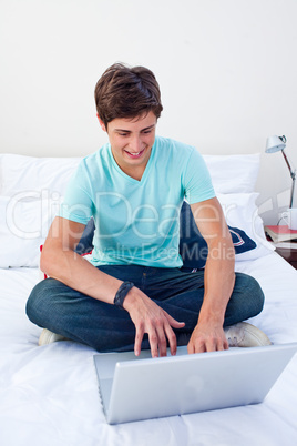 A teenage guy sitting on his bed using a laptop