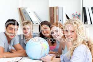 Smiling teenagers in a library working with a terrestrial globe