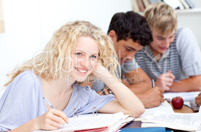 Happy teen girl studying in the library with her friends